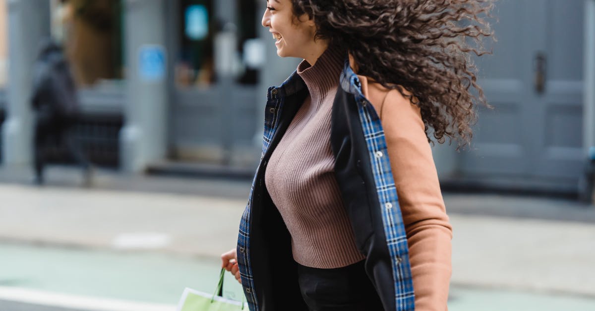 Are Koopa the Quick times constant? - Positive young ethnic female with flowing hair carrying shopping paper bags while quickly crossing road and looking away