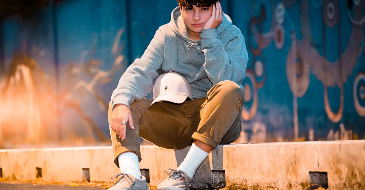 Are levels after 40 cap but before beating Keener lost? - Ground level of crop stylish male adolescent in contemporary wear with cap sitting on barrier leaning on hand and looking at camera in evening