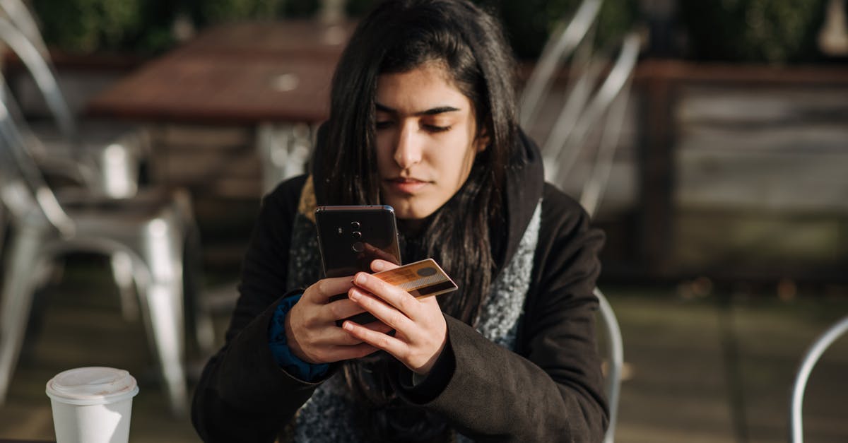 Are the cards a one-time use? - Young ethnic female purchaser with credit card shopping online on mobile phone at table with takeaway hot drink in cafeteria