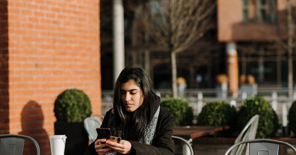 Are the cards a one-time use? - Young attentive Hispanic female buyer with cellphone and credit card shopping online in urban cafeteria