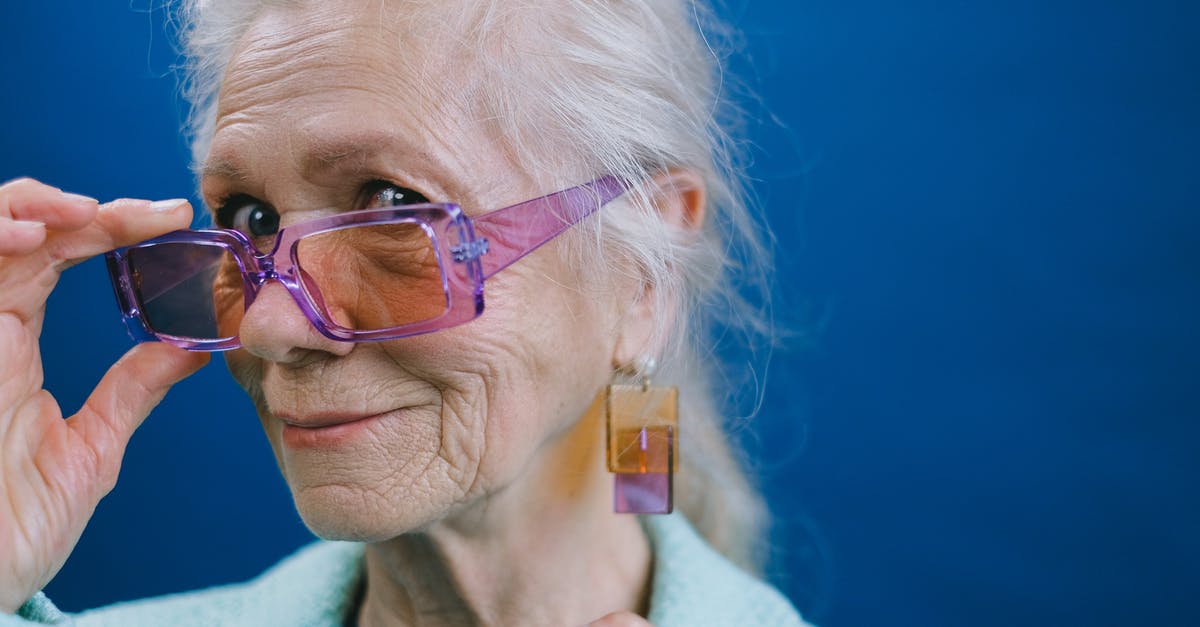 At what age an heir become the ruler? - Portrait of elegant smiling gray haired elderly female wearing purple sunglasses and earrings looking at camera against blue background