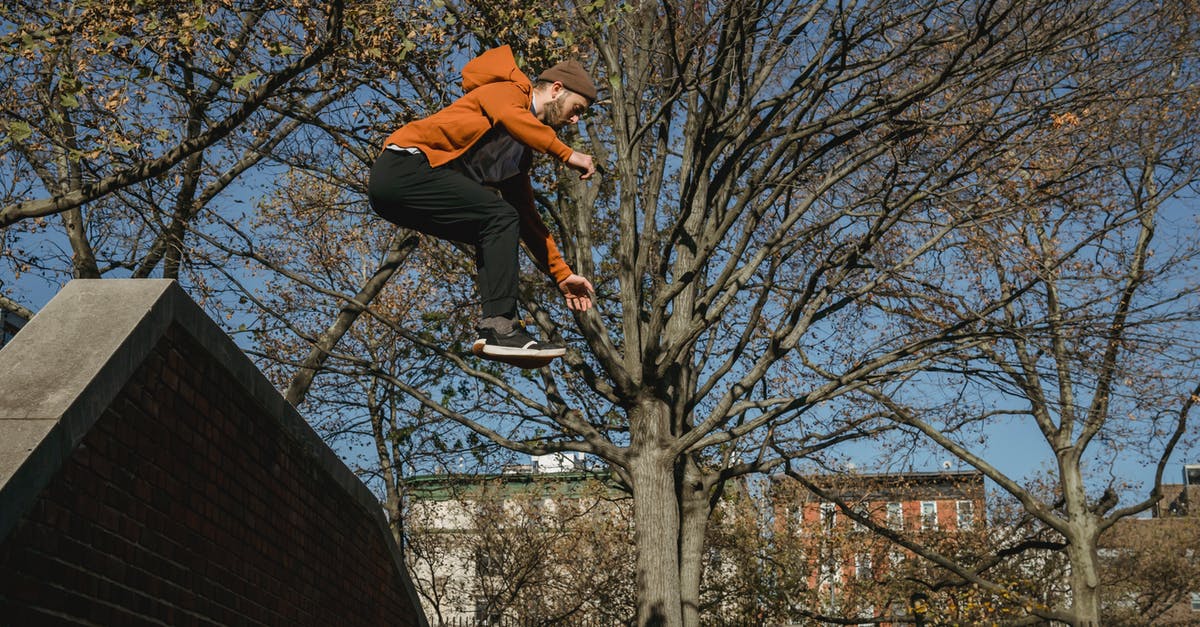 Autumn season challenge - Energetic man jumping from brick wall in city park