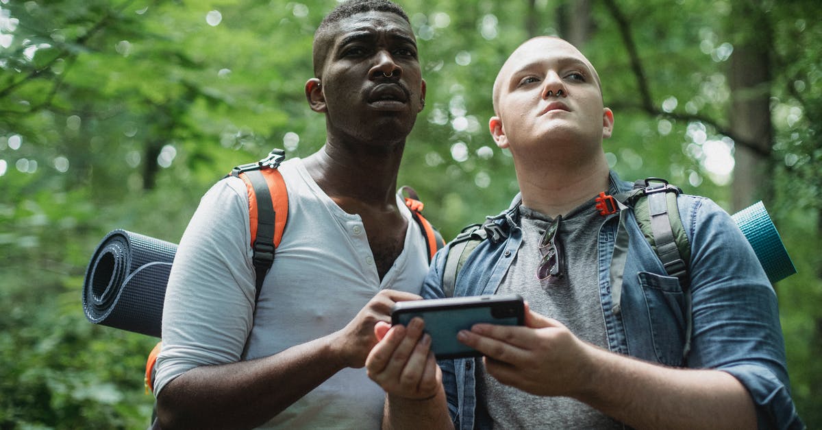 Best way to find treasure maps - From below of diverse lost travelers with backpacks exploring woodland and searching way in cellphone