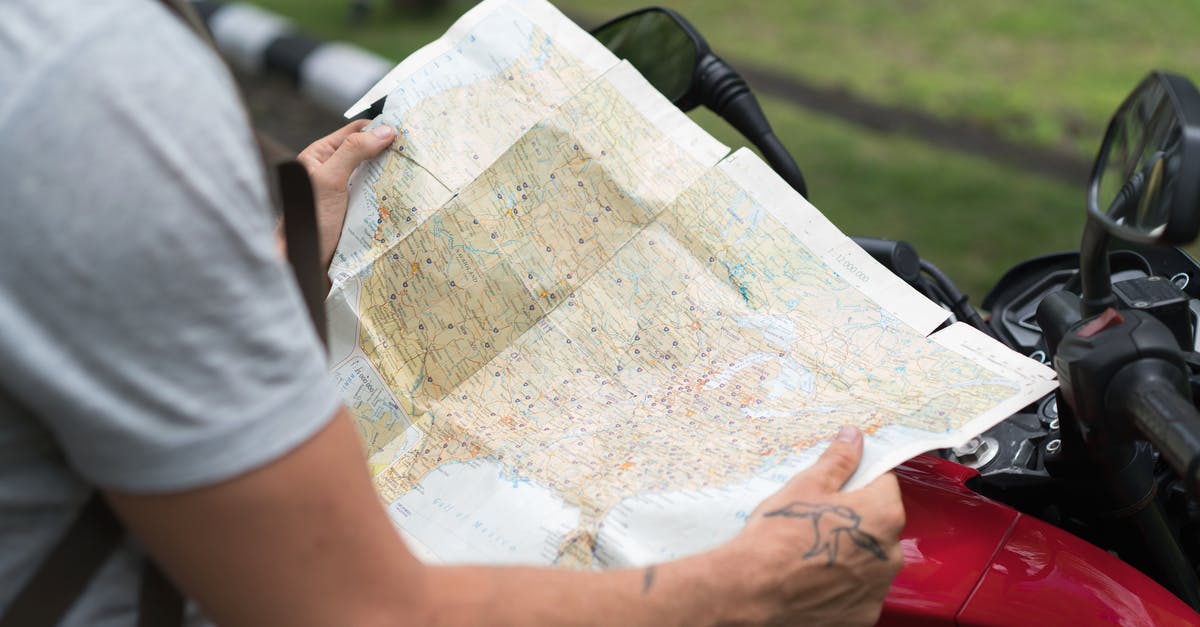 Best way to find treasure maps - Side view of crop unrecognizable male in casual clothes with backpack sitting on motorcycle while studying city map on street