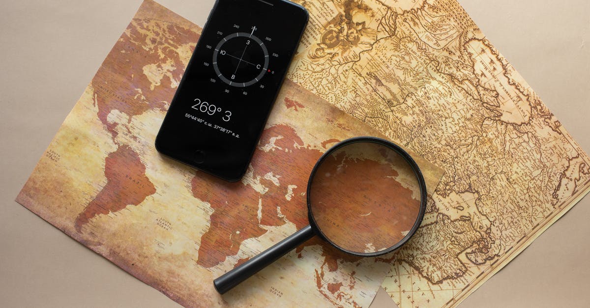 Can't find my horse? - Top view of magnifying glass and cellphone with compass with coordinates placed on paper maps on beige background in light room