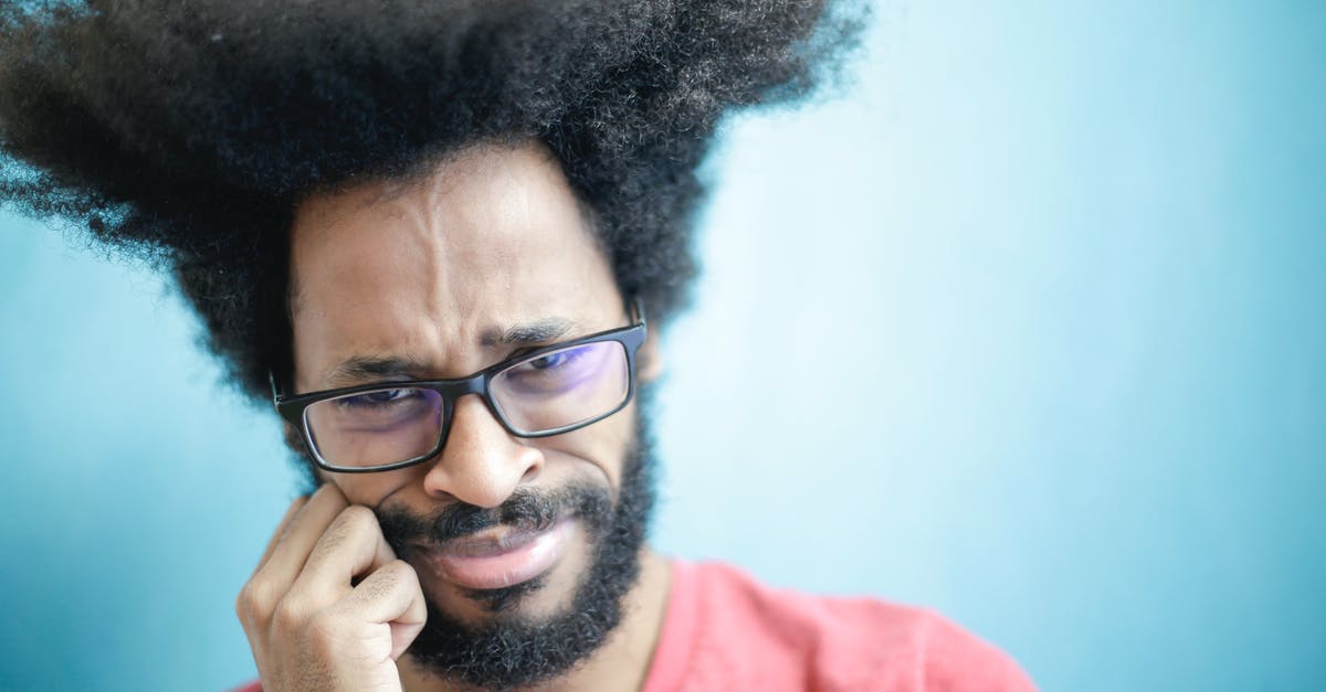 Can't get into 3rd puzzle - Suspicious young bearded ethnic male with creative Afro hairstyle wearing eyeglasses and pink t shirt touching cheek and looking at camera with uncertain or doubt expression