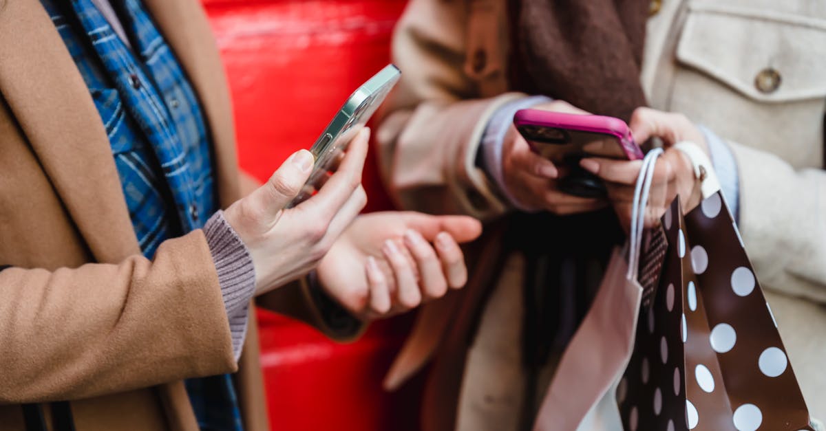 Can't gift a game to a friend through Battlenet app - Crop faceless female friends in stylish outfits using smartphones while standing on street near red wall with shopping bags