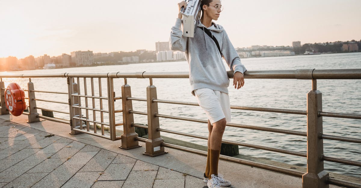 Can't hear any sound on True Skate - Full length fit ethnic male skater riding skateboard on city embankment with old fashioned tape recorder on shoulder in early evening