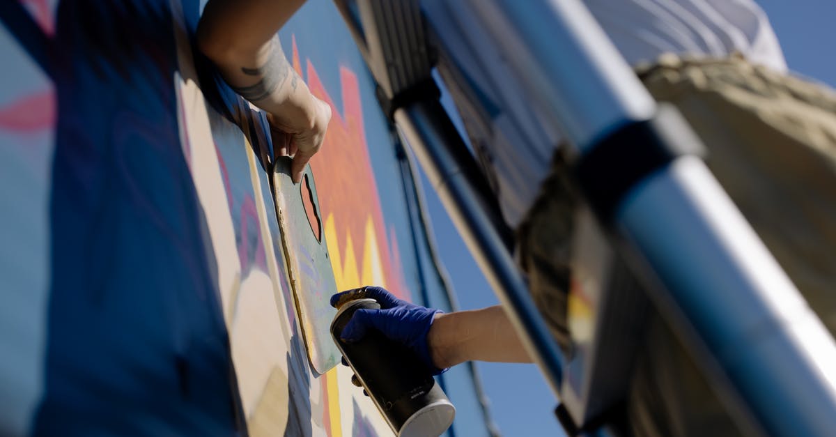 Can a city exploit tiles from two provinces? - From below of crop unrecognizable person in casual clothes and gloves using spray can while painting graffiti wall standing on ladder