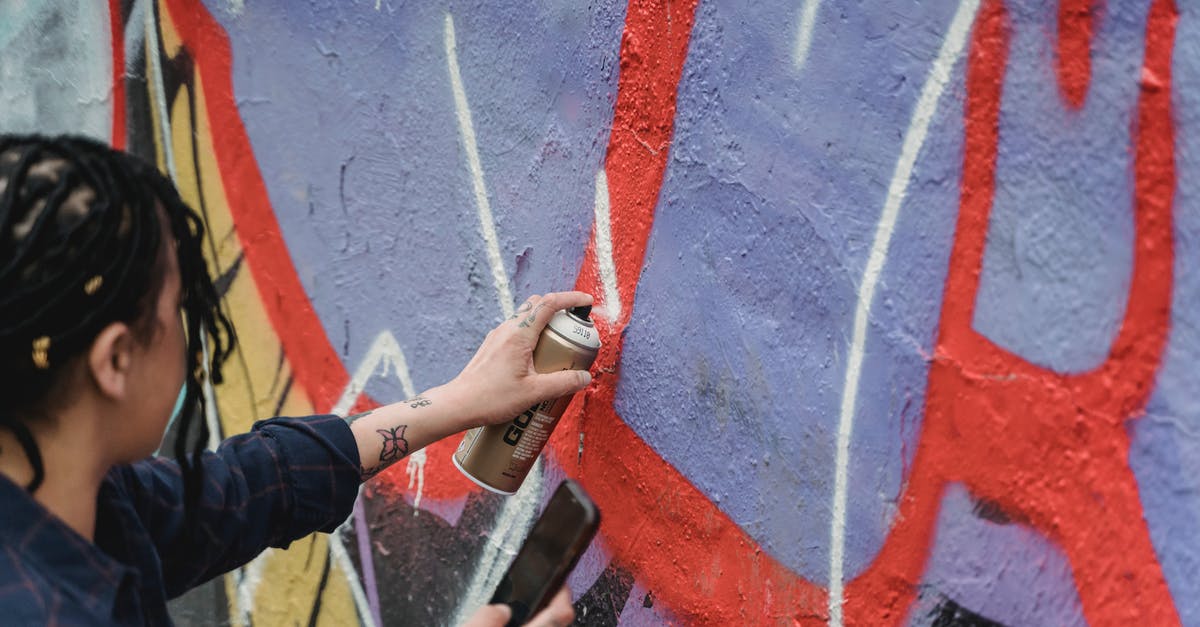 Can a city exploit tiles from two provinces? - From above side view of crop faceless female artist with braided hair painting graffiti on wall while standing on street