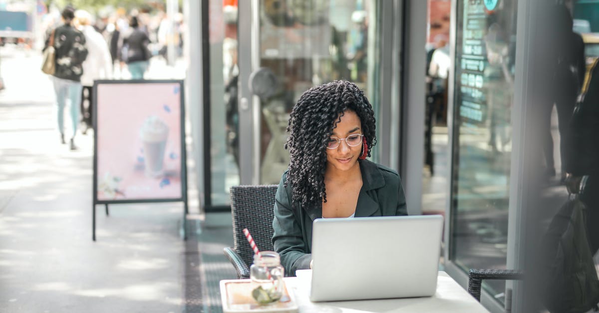 Can AC Black Flag share files with AC Rogue? - High angle of pensive African American female freelancer in glasses and casual clothes focusing on screen and interacting with netbook while sitting at table with glass of yummy drink on cafe terrace in sunny day