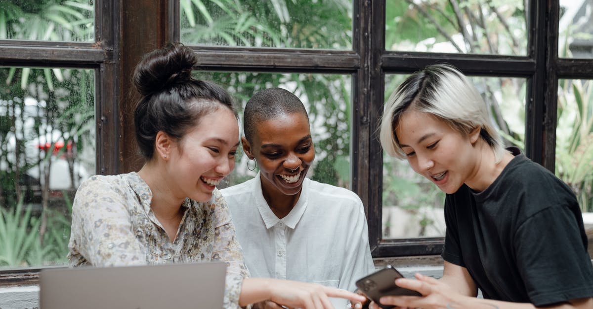 Can AC Black Flag share files with AC Rogue? - Cheerful young diverse female friends laughing while watching funny video on smartphone during coffee break in cozy cafe