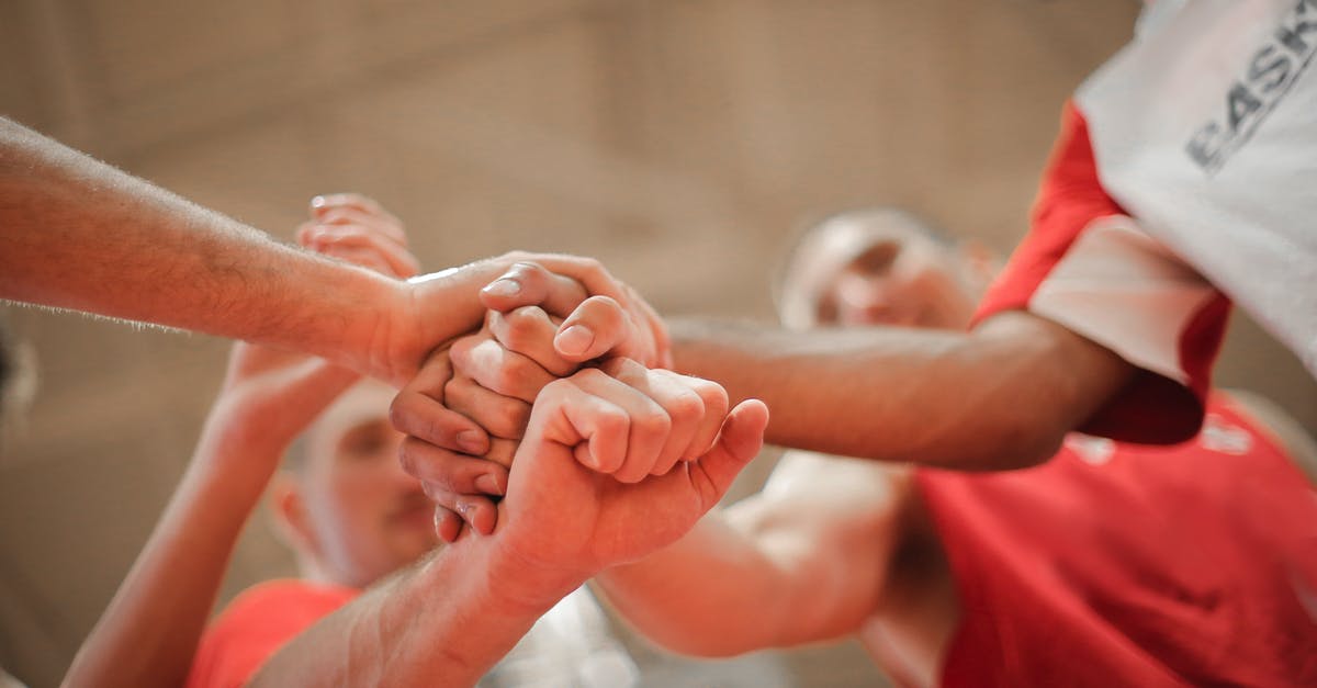 Can I download a game from another PSN to my PSN - From below of crop multiethnic team of professional basketball players gathering and putting hands together while standing on playground before game