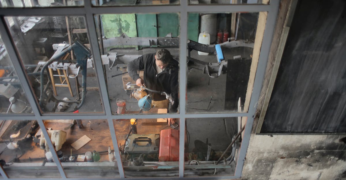 Can I install Assassin's Creed through Steam? - Through window view of male worker in casual uniform standing near workbench and working with instruments in grungy workshop