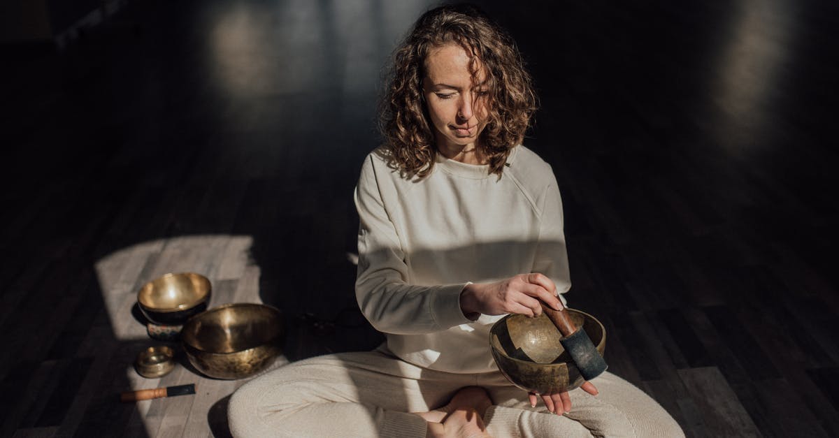 Can I play cross-platform multiplayer? - Female sound therapist sitting with crossed legs on parquet while playing singing bowl with mallet during meditation practice