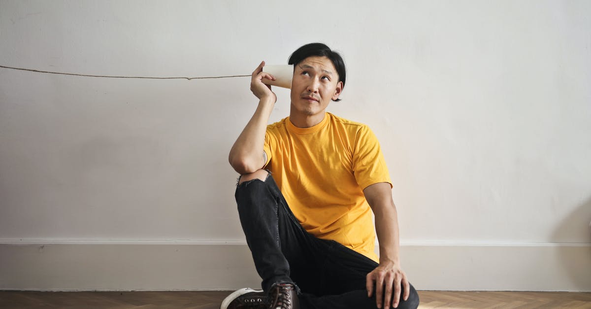 Can I play cross-platform multiplayer? - Asian guy in casual clothes using paper cup with thread as telephone while sitting on floor against white wall