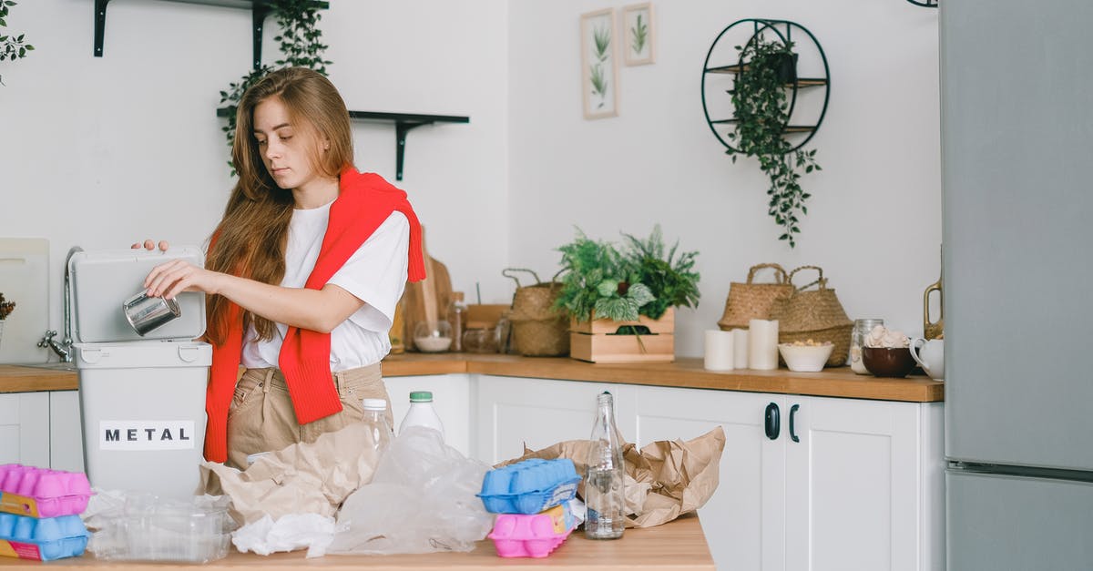 Can I save my highlights? - Young responsible female standing in kitchen and putting tin can into bucket while sorting trash