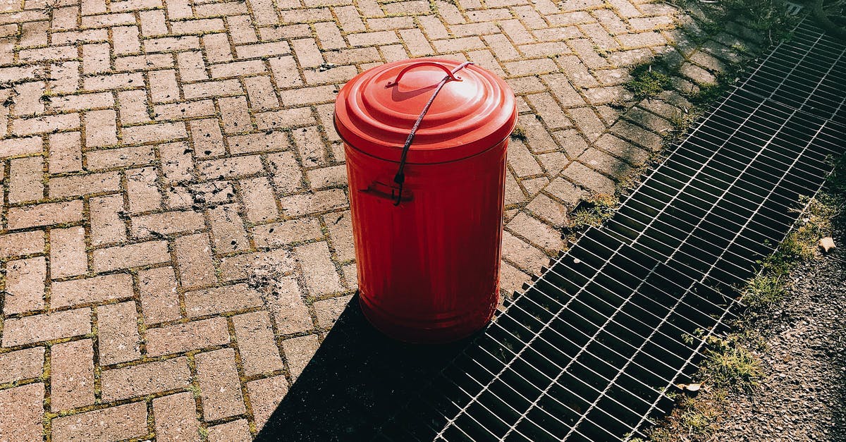 Can I undo red choices? - High angle of red metal trash can placed on pavement near sewer grates in city street in sunny summer day