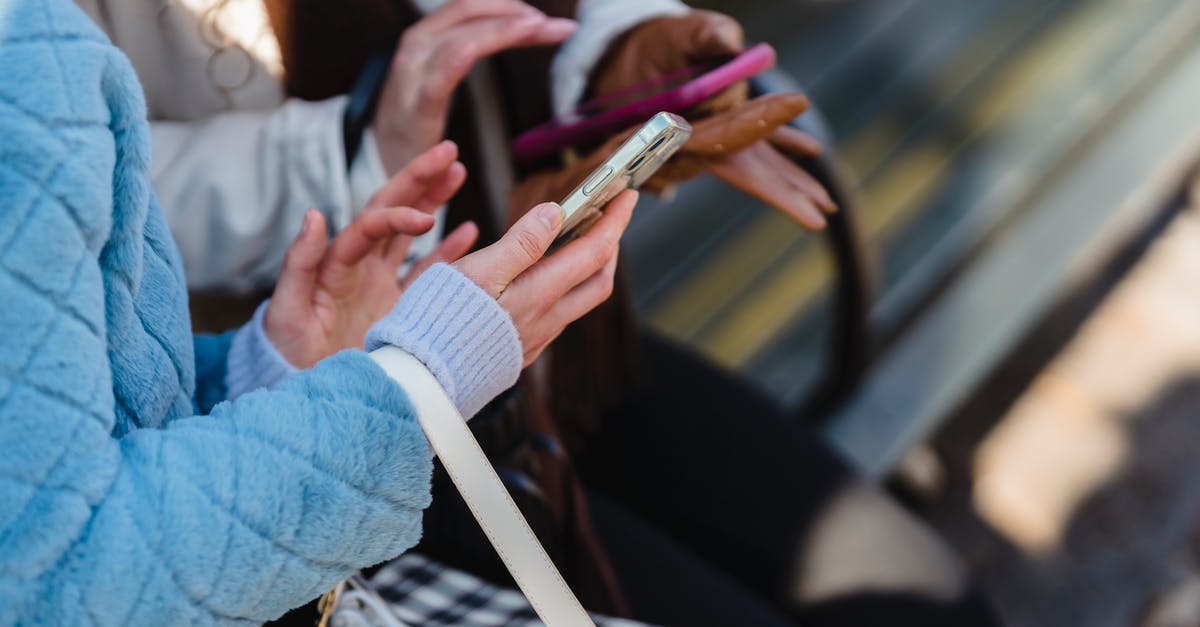 Can my friend play Street Fighter V online from shared library? - From above of crop anonymous friends sharing information on mobile phones in park in daytime on blurred background