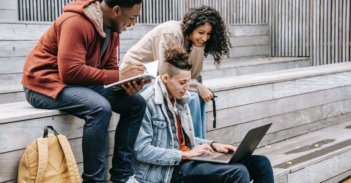 Can my friend play Street Fighter V online from shared library? - Young content multiracial friends browsing internet on netbook while doing homework on urban staircase in daylight