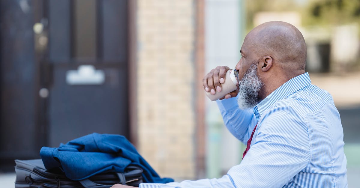 Can you break doors by throwing things at them? - Side view of elderly bearded African American man in trendy outfit sitting at table with jacket and handbag and drinking beverage from tin can in veranda of cafe