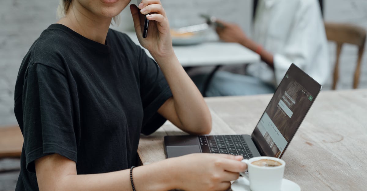 Can’t talk to my teammates - Crop Asian lady in black tee making phone call while sitting at table with coffee and laptop in cafe