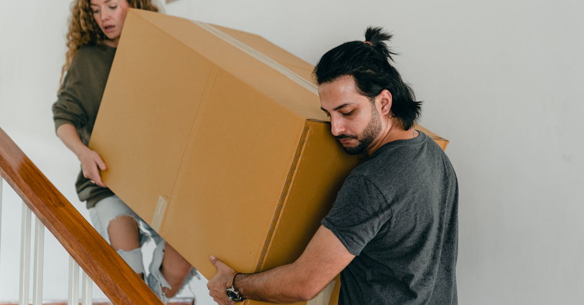 Copy and change item names in chest - Focused couple in casual clothes carrying big carton box together down stairs in new house while moving personal items