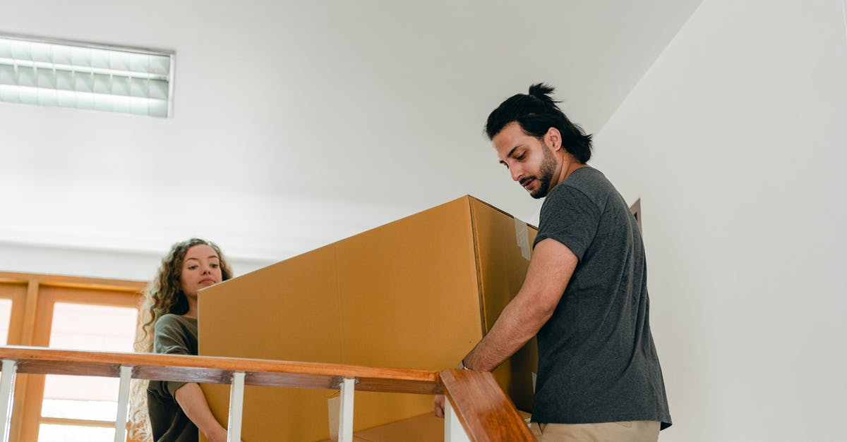 Copy and change item names in chest - From below of couple in casual clothes carrying big carton box together while moving packed personal items into new apartment