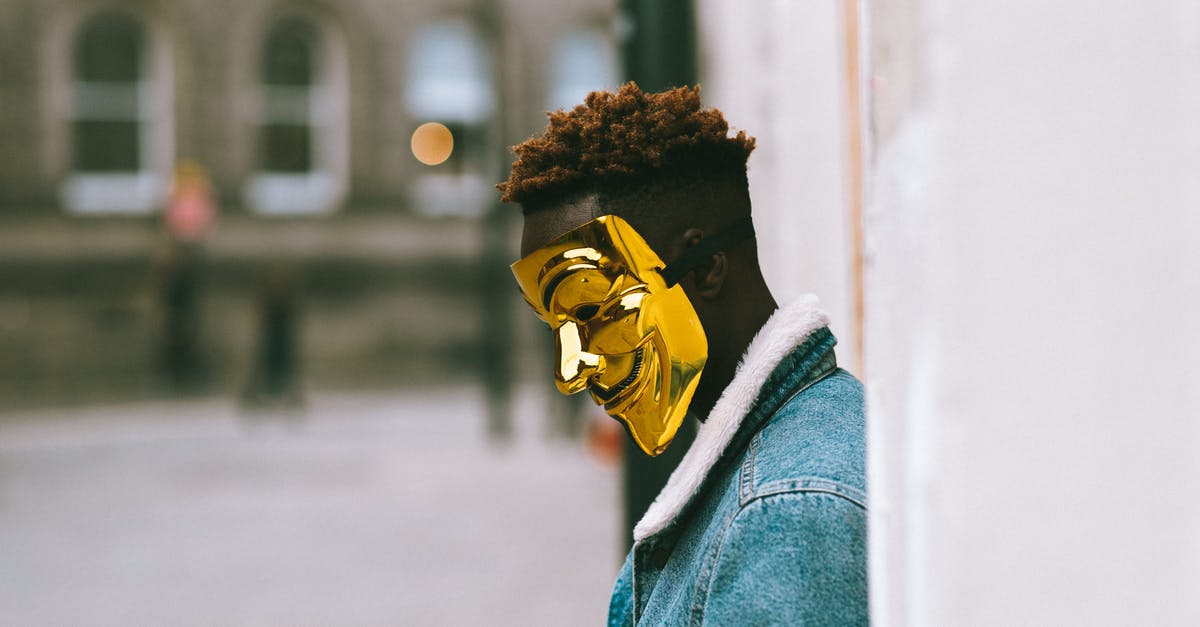 Corruption of GLaDOS - Side view of thoughtful African American activist wearing golden Anonymous mask as symbol of protest against current state policy standing near building on city street in daytime