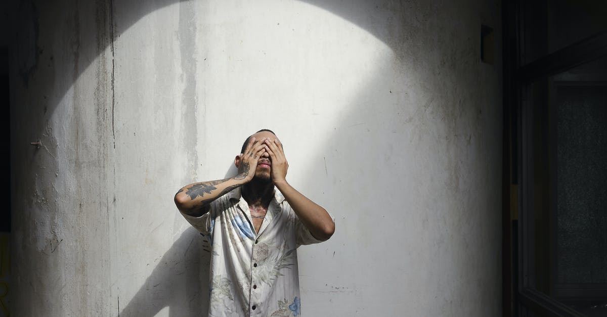 Custom Data model shows old textures but slighty darkened - Young man with short brown hair and tattoos on arm in shirt standing near white wall and closing eyes with hands