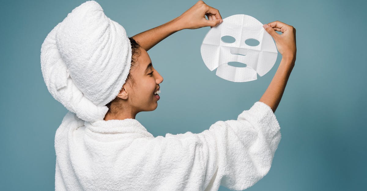 Daily challenge not showing - Back view of happy young African American female in bathrobe with towel on head smiling while demonstrating skin care mask against blue background