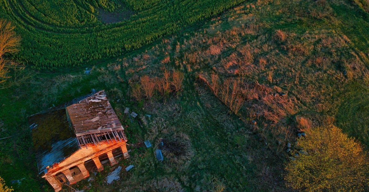 Destroy all farms or not? - Aerial view of abandoned house with destroyed roof located on green grassy field in countryside during sunset