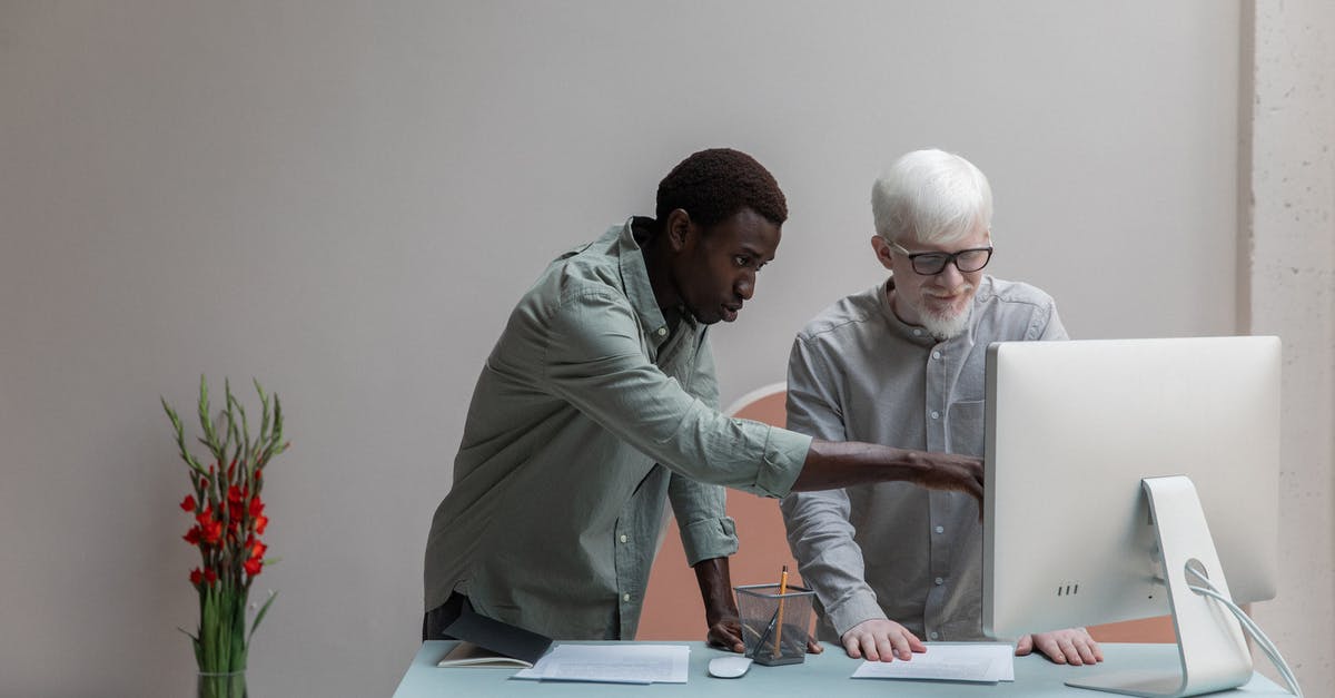 Differences between PC and PS4 updates? - Concentrated African America man and albino male standing near table while browsing computer during work in modern office with flower