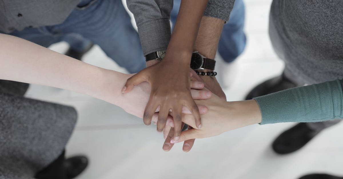 Discord-Minecraft integration - Crop from above of faceless multiracial friends in casual clothes uniting hands after coming to agreement while standing on light grey ceramic floor