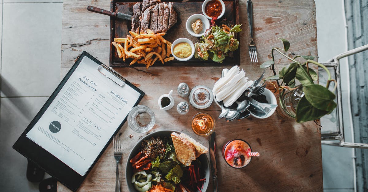 Do ghouls need to eat and drink to survive? - Top view of wooden table with salad bowl and fresh drink arranged with tray of appetizing steak and french fries near menu in cozy cafe