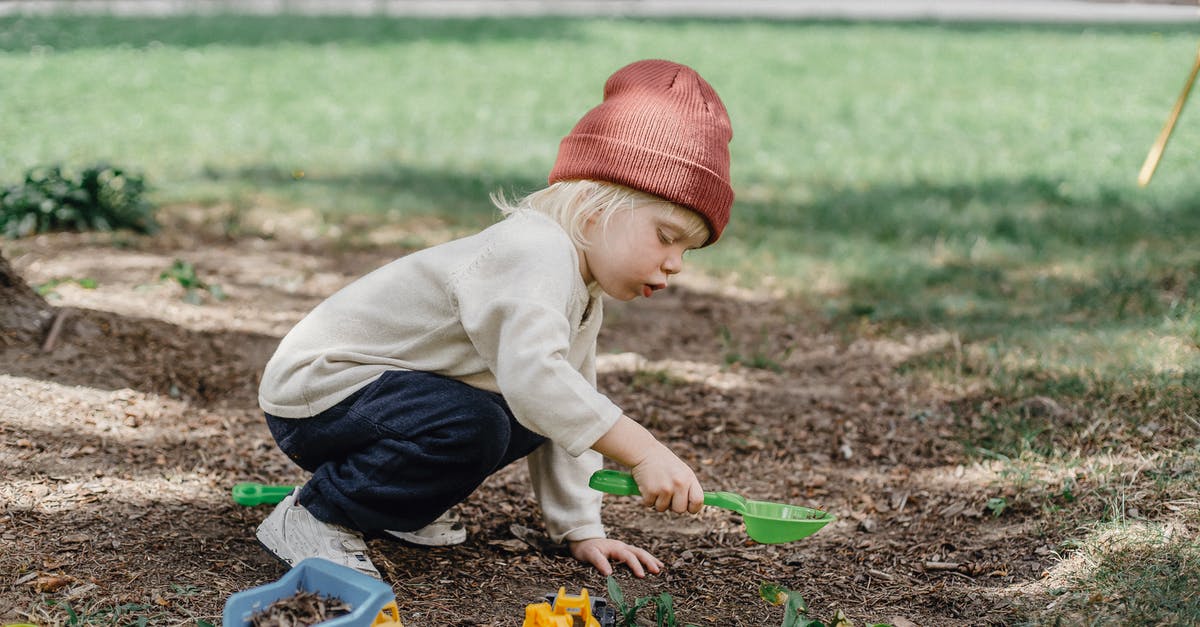 Do I have to play Persona games in order? - Side view of little boy in casual clothes and brown hat playing with plastic toys in backyard