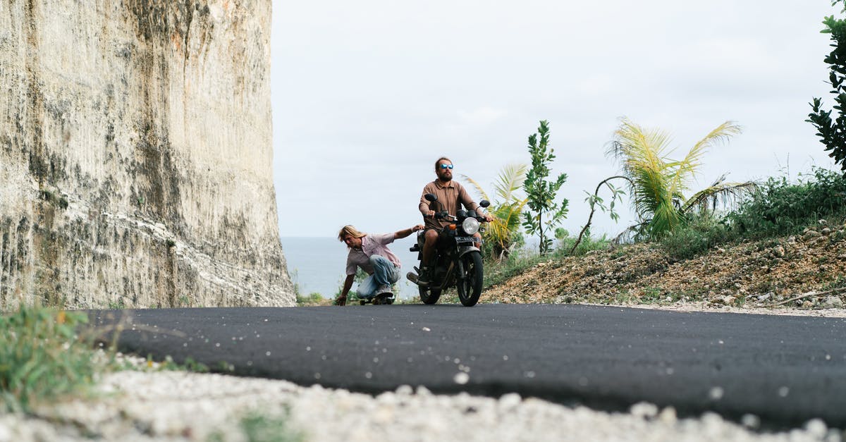 Do kills through Zin's 'Recite' ability grant experience? - Full length male driver of motorbike riding friend in sitting position on skateboard while friend holding seat and touching surface of road with another hand