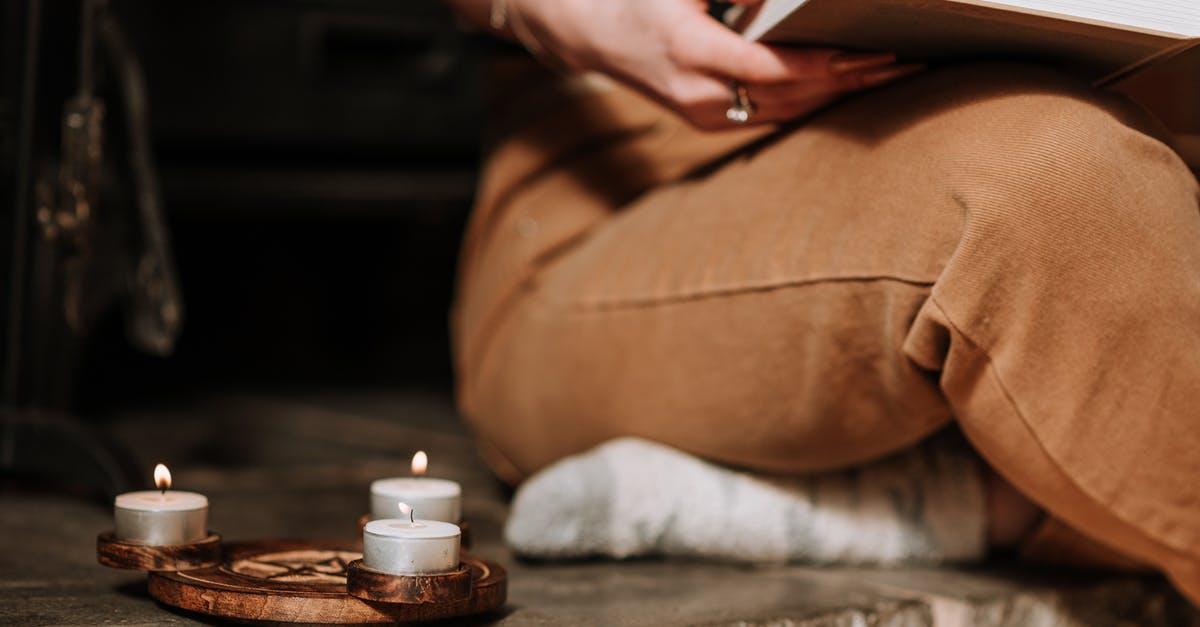 Do the Skaal believe in reincarnation or not? - Unrecognizable mysterious female with book sitting in aged house near small burning candles placed on metal surface with spiritual symbol