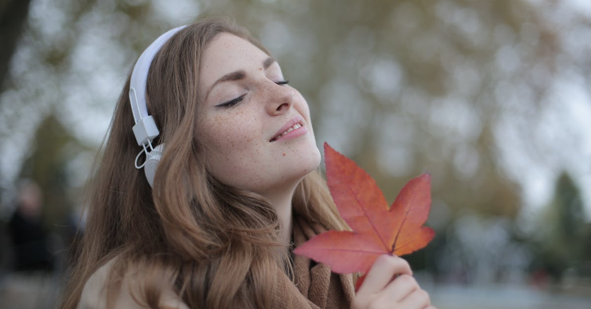 Do you fall faster alone in Apex Legends? - Young satisfied woman in headphones with fresh red leaf listening to music with pleasure while lounging in autumn park