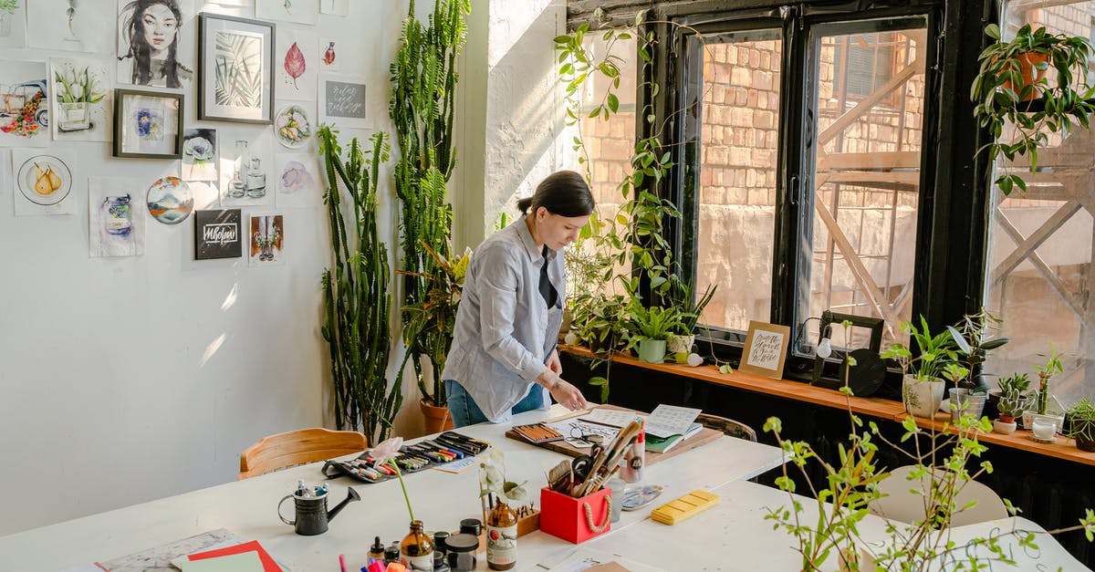 Does 3DS Streetpass work in different regions? - Side view of female designer creating drawings at desk with collection of felt pens and papers near wall with artworks and plants on windowsill in daylight