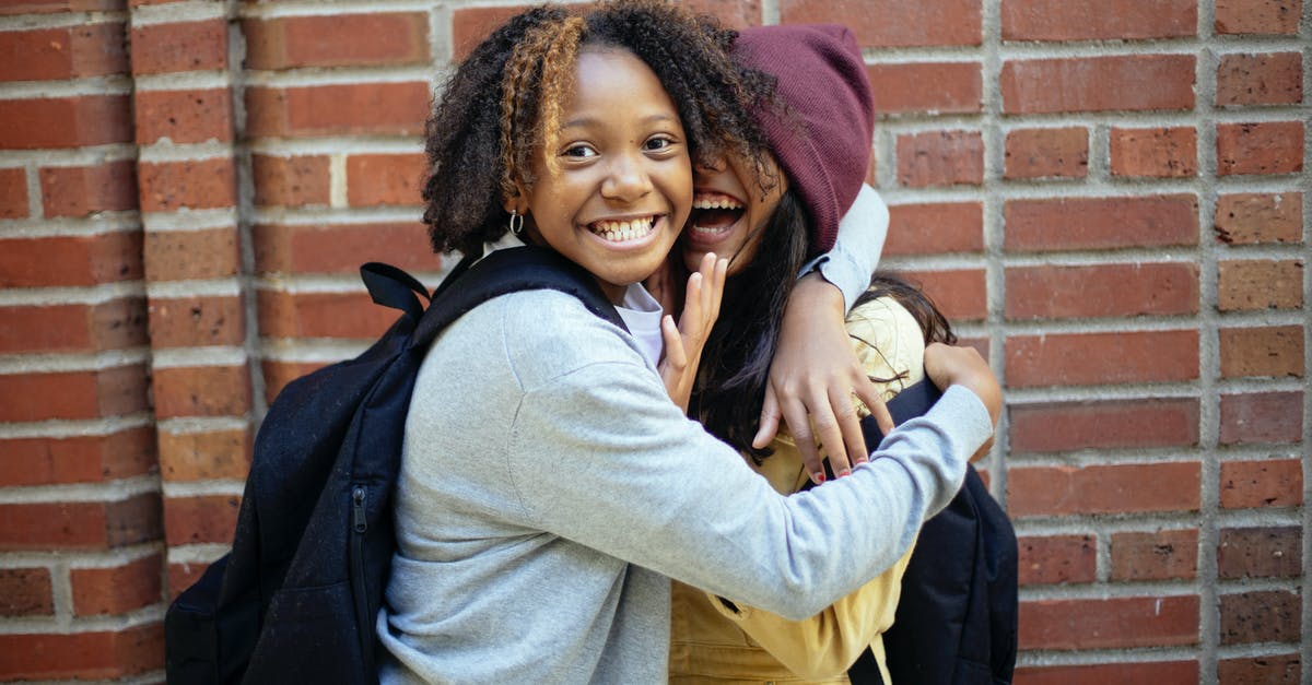 Does A Hat In Time have co-op? - Cheerful African American girl in casual clothes hugging friend while having fun near brick wall