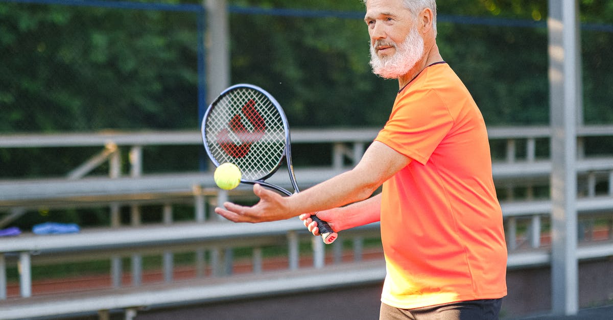 Does age matter when it comes to tennis skills? - Side view of cheerful senior sportsman standing with ball and racket and preparing to serve ball on court in daytime