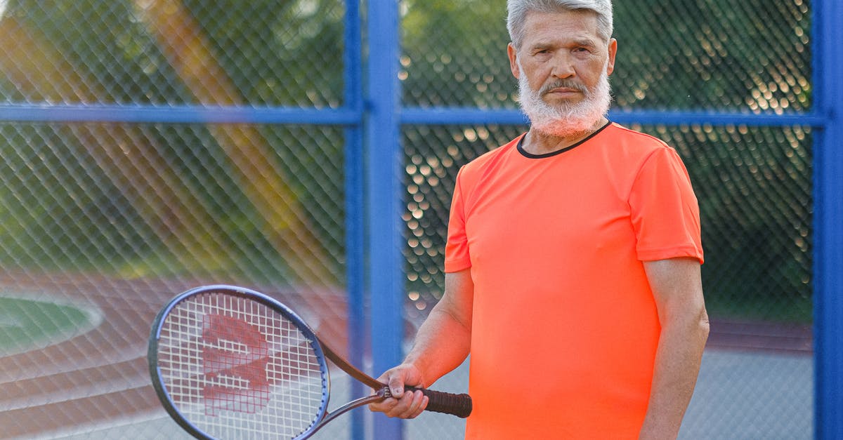 Does age matter when it comes to tennis skills? - Focused senior sportsman in sportswear standing with racket while playing tennis on sports ground in sunny day