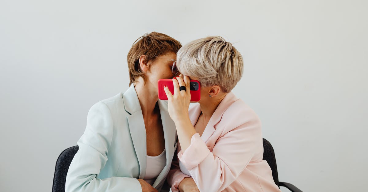 Does hiding in dead bodies work against enemies? - Women in Blazers Sitting Beside and Hiding a Kiss Behind Red Mobile Phone