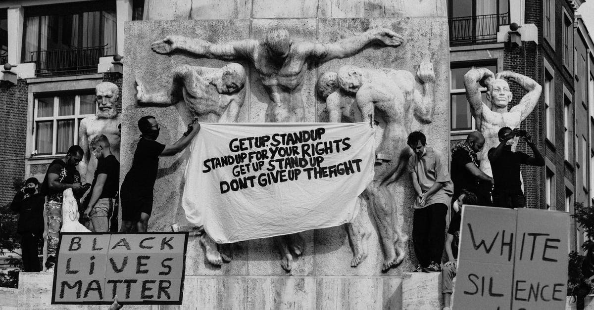 Does location actually matter? - Black and white of crowd of people standing on city street with carton boards during social protest