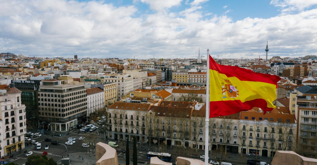 Does National visistor center affect all cities? - Drone view of Spanish city with aged buildings and national flag under cloudy blue sky