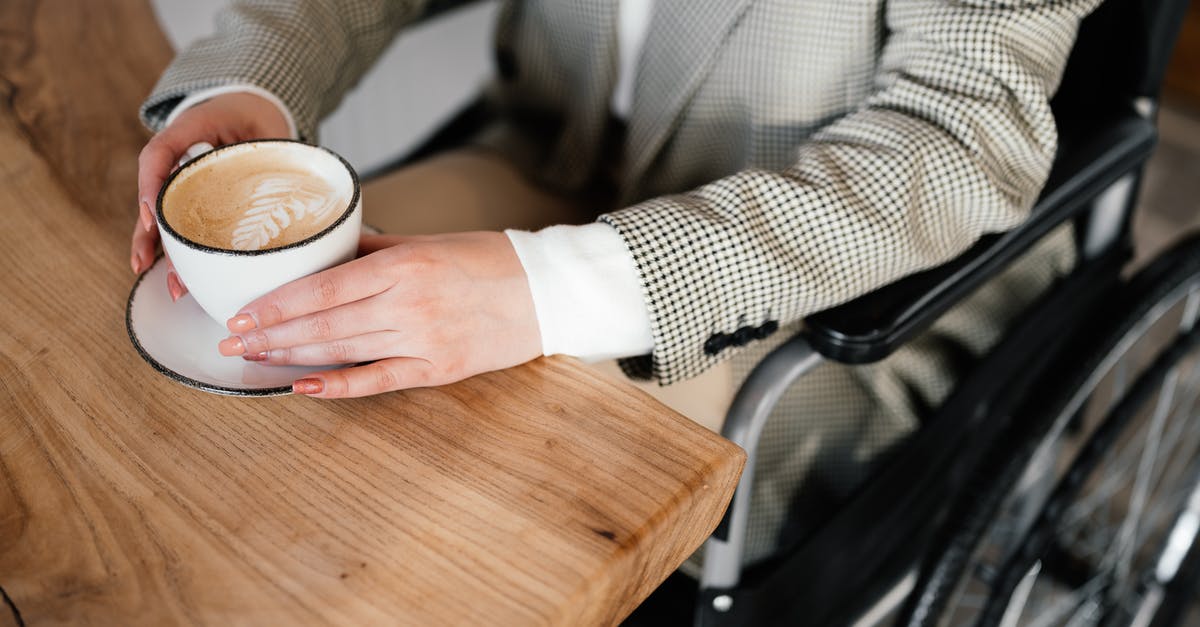 Does stun from artillery disable crew perks? - From above of unrecognizable female sitting in wheelchair at wooden table with cup of latte while spending time in cafe