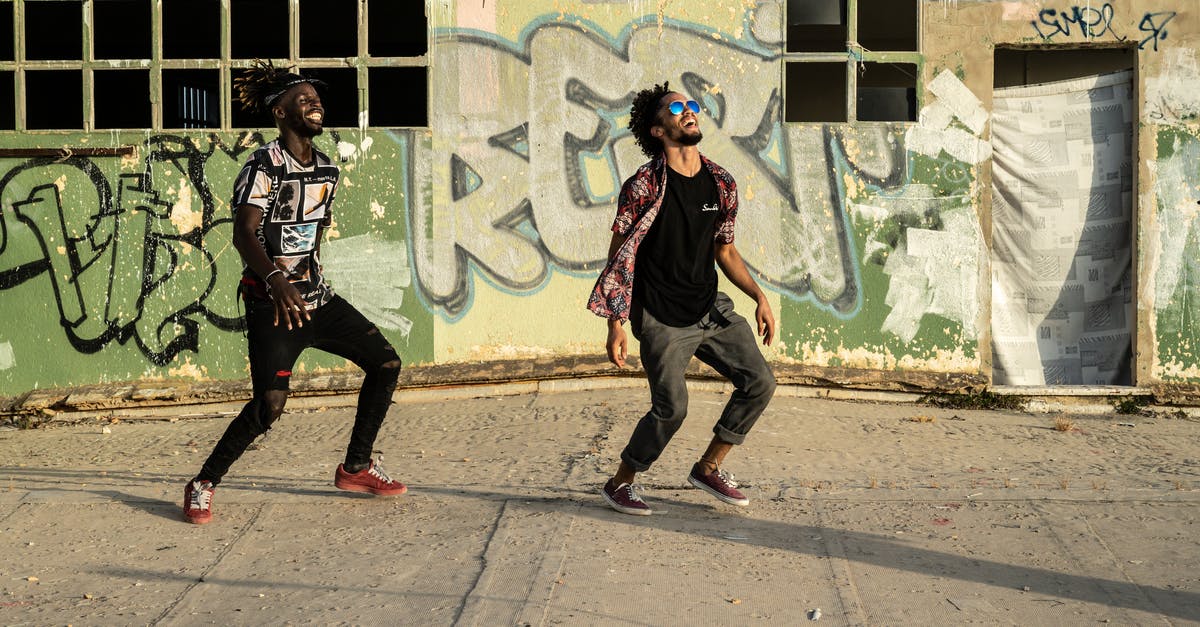 Don't have the needed software to perform this action? - Cheerful young ethnic men dancing on street near graffiti wall