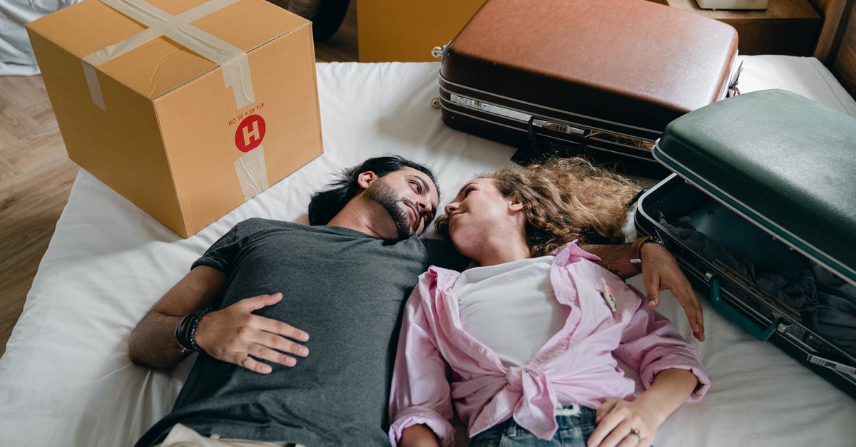 Don't Starve Together - how to find each other - From above of young ethnic bearded man and woman with curly hair looking at each other and lying on bed among suitcases and cardboard boxes with stuff while moving in new apartment together