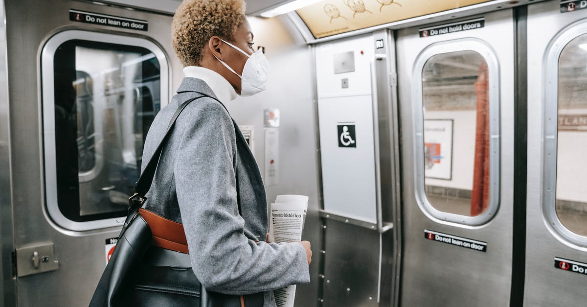 Dragon riding tamed Wolf problem - Back view contemplative young African American female in stylish wear and face mask standing with handbag and newspaper and riding subway train